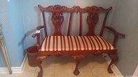Carved wood settee with striped cushioned seat showing full front and armrests.