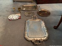 Photo showing all items laid out on floor: three silver-plated trays, two metal trivets, two silver-plated wine goblets.