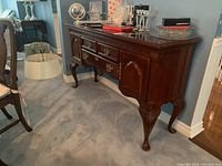 Front left angle view showing carved edging, two small top drawers, larger central drawer, brass bail pulls and cabriole legs