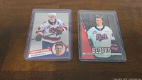 Two Connor Bedard hockey cards in plastic sleeves on a wooden surface, featuring his 2023 and 2020 cards.