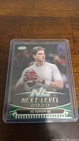 Front view of a Joe Burrow 2020 Next Level rookie card in protective sleeve on wooden surface.