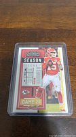 Photo of Patrick Mahomes II Panini Contenders Season Ticket card encased in plastic sleeve on wooden surface.