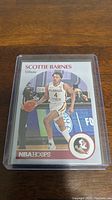 Front of Scottie Barnes NBA Hoops Tribute rookie basketball card in plastic holder on wooden surface.
