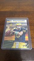 Front view of 1999 Tom Brady Michigan football card in clear protective case showing player image, year, and team details.