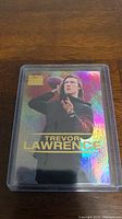 Close-up photo of Trevor Lawrence rookie football card with holographic effect inside a protective plastic case.