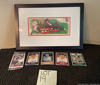 Framed Mark McGwire commemorative envelope alongside five vintage baseball cards on display surface with lot number sign.