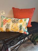 Two decorative pillows side by side: one solid coral square pillow and one rectangular tropical pineapple themed pillow