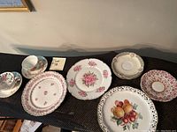 Overview of all 10 pieces in the lot including cups, saucers, and plates with various floral and fruit patterns and gold trim.
