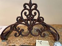Front view showing decorative fleur-de-lis design and base curved arms of the cast iron hose holder.
