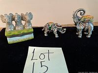 Three-elephant ceramic trinket box along with two small pewter jeweled elephant figurines shown on black surface.