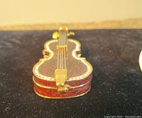 Close-up of the front of the small cello-shaped jewelry box showing red finish and jewel encrustations.