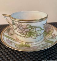 Close-up of a single tea cup showing hand-painted floral design with gold trim on the rim and handle.