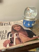 Photo showing the snow globe next to the newspaper article featuring Peggy Fleming on the cover, highlighting the association with the Olympic gold medalist.