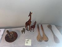 Full lot overview showing two wooden giraffe figurines, two small metal animal figurines, and three hand carved wooden serving utensils.