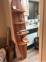 Full view of wooden surfboard bookshelf leaning against wall by kitchen counter