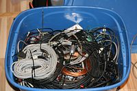 Top view of the blue plastic tub filled with various black and grey cables, connectors, and copper wire inside.