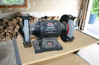 Front angle view of Jobmate dual 6 inch bench grinder showing one coarse grinding wheel and one finer wheel with protective guards and tool rests on a table.