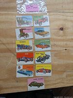 Top view of all 11 vintage Topps 1954 World on Wheels trading cards on wooden table showing various classic cars and motorcycles.