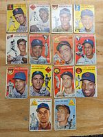 Full view of the 14 vintage 1954 Topps baseball cards laid out in a grid on a wooden surface, showing player portraits and some wear and corner damage.
