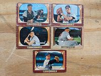 Five 1955 Bowman baseball cards laid out on wood surface showing front portraits and player names: Billy Pierce, Chico Carrasquel, Al Aber, Wes Westrum, Ralph Beard.
