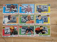 Lot of nine 1955 Topps All American football cards laid out on wooden surface, featuring Vic Hanson, Eddie Tryon, Benny Friedman, Bruiser Kinard, Bobby Dodd, Ralph Kercheval, Angelo Bertelli, Cas Myslinski, and Aaron Rosenberg.