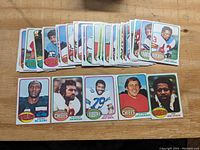 Photo showing about 40 football cards arranged on a wood surface, with the front row highlighting cards of Mel Blount, Len Dawson, Gene Upshaw, and others.