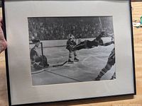 Photo showing the framed black and white vintage photograph with a hockey scene of Bobby Orr's goal, white matte border, simple dark frame.