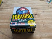 Full unopened box of 1990 Fleer Premier Edition Football Player Photo Cards on wooden table showing front and top graphics.