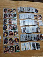 Wide view of multiple stacks of 1990 Hoops basketball cards spread on a wooden surface, showing various player cards face up.