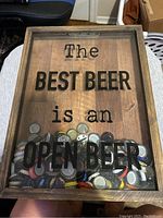 Wooden shadow box with a glass front featuring the printed phrase 'The BEST BEER is an OPEN BEER', filled with assorted beer bottle caps inside.
