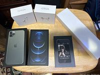 Photo of five empty Apple product boxes arranged on a wooden table including iPhone 12 Pro, iPhone 5, two AirPods Pro, and a long white box.