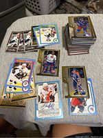 Photo showing a pile of assorted hockey cards on a cloth surface including several gold-bordered cards, player cards from Pittsburgh Penguins, Colorado Avalanche, Calgary Flames, Edmonton Oilers, and cards with autograph signatures.