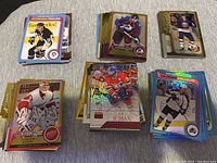 Photo of various hockey cards organized in small piles on a surface. Cards feature players from teams including Pittsburgh Penguins, Colorado Avalanche, Detroit Red Wings, Montreal Canadiens, New York Islanders. Cards have colorful and holographic finishes.