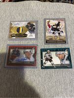 Four hockey cards in plastic sleeves on fabric surface showing autographs, memorabilia patches, and player imagery.