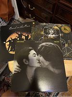 Three vinyl record covers: Band on the Run, Double Fantasy, All Things Must Pass visible on a small table with part of a room background.