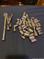A collection of multiple 1/4 inch drive metal sockets and two ratchet wrenches arranged on a fabric surface.