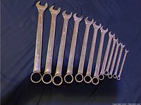Photo showing full set of 12 metal combination wrenches arranged from largest to smallest on dark fabric background.