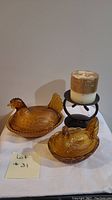 Full view of the two amber glass nesting hen covered dishes and the candle on a metal holder.