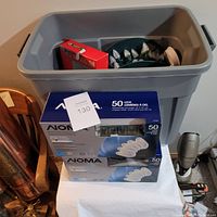 Full bin showing multiple coiled Christmas light strands, two blue NOMA clip boxes, and one red box inside plastic bin on white cloth