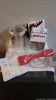 Entire lot showing all items including towels, glass tea cups, silver canister, tea strainers, and red utensils in original packaging.