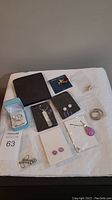 Photo showing brown wallet, multiple sets of silver based earrings, silver necklace pendants, and other silver jewellery pieces arranged on a white surface.