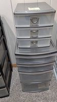 Full view of two stacked plastic drawer bins: smaller one with 3 small drawers on top of larger one with 4 drawers (2 small, 2 large). Grey handles and translucent drawers.