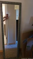 Full view of the rectangular long mirror showing its reflective surface, pewter-colored ornate frame, and size relative to a door and floor.