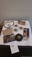 Overview of lot items on white cloth: jewelry pieces, small purse, mirrored notepad, keychains, and other small accessories