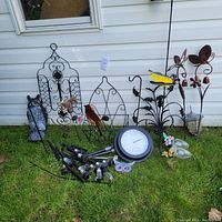Wide view of all garden metal decor items on grass in front of white siding wall