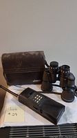 Photo of vintage binoculars with carrying case and transmitter on cloth surface