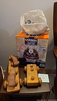 Two wooden toy car sets and a vintage Smurf collection in a plastic bag placed on top of a Lionel 100th Anniversary Train Alarm Clock box.