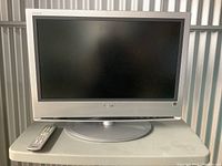Sony Bravia 26 inch TV with silver bezel and base stand, screen turned off, remote placed in front.