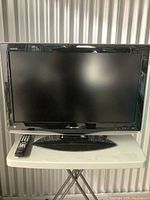 Front view of the 31-inch Sharp Aquos television powered off, showing the screen and bezel with remote on the table.