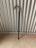 Full-length view of cane leaning against corrugated metal background on concrete floor